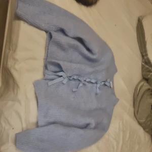 Ljusblå stickad kofta med knytband - Superfin ljusblå stickad kofta med långa ärmar och snygga knytband framtill. Koftan är ribbstickad och har en mysig, lite loose passform. Perfekt att slänga på sig när det är kyligt ute. Passar dig som gillar söta detaljer och en chill vibe. 300 kr