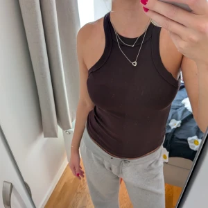 Mörkbrun ribbad linnetopp - Snygg mörkbrun ribbad linnetopp med tight passform och sportig skärning vid axlarna. Toppen är ärmlös och har en rund halsringning. Perfekt att styla med jeans eller kjol för en cool vardagslook.