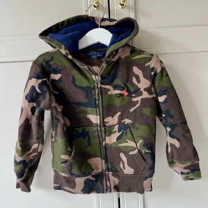 Camo hoodie från Polo Ralph Lauren - Säljer en camouflagemönstrad hoodie från Polo Ralph Lauren i storlek 3/3T. Tröjan har dragkedja, huva med blått foder och klassisk logga på bröstet. 