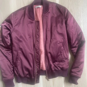 Vinröd bomberjacka - Snygg vinröd bomberjacka från Soaked i storlek XS. Jackan har ribbade muddar, dragkedja i guld och två fickor framtill. 