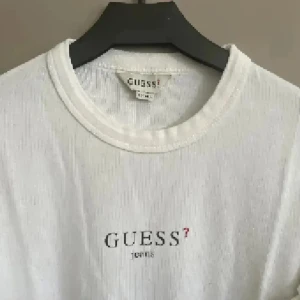 Vit långärmad tröja från Guess - Vit långärmad tröja från Guess med enkel och clean design. Tröjan har rund halsringning och diskret Guess Jeans-logga framtill. Perfekt till jeans eller kjol för en stilren look. Tillverkad i mjuk bomull som känns skön mot huden.
