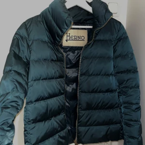 Mörkgrön dunjacka från Herno - Snygg mörkgrön dunjacka från Herno med quiltad design och hög krage. Jackan har dragkedja framtill och är lättviktig men ändå varm tack vare Polar-Tech och dunfyllning. Perfekt för kalla dagar och har en clean, stilren look.