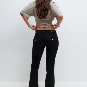 Svarta bootcut jeans från Gina - Säljer ett par svarta bootcut jeans från Gina med klassisk femficksdesign och snygga detaljer på bakfickorna. Jeansen har låg midja, säljer pga att de blivit för små.