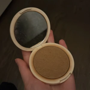 Bronzer från H&M Beauty - Snygg bronzer i en rund, beige kompakt med spegel från H&M Beauty. Färgen är varm och gyllenbrun, perfekt för att ge ansiktet en solkysst look. Smidig att ha med i väskan tack vare den kompakta designen och inbyggd spegel. 