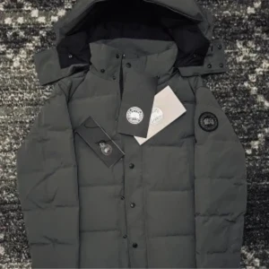 Mörkgrå pufferjacka från Moose Knuckles - Snygg mörkgrå pufferjacka från canada gosse med huva och svart logotyp-patch på ärmen. Jackan har dragkedja och knappar framtill, samt quiltad design som ger en cool och modern look. Perfekt för kalla dagar när du vill hålla stilen.