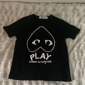 Svart t-shirt Comme des Garçons Play - Svart t-shirt från Comme des Garçons Play med ikoniskt stort hjärta med ögon och vit text på bröstet. Klassisk rund hals och korta ärmar. Vid fler frågor eller funderingar är det bara att skriva!