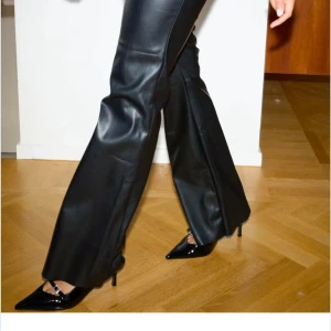 Svarta bootcut byxor i skinnimitation - Snygga svarta byxor i skinnimitation med bootcut och låg midja. Byxorna har en slät yta, markerade sömmar över knäna och en klassisk stängning framtill. Perfekta för dig som vill ha en edgy och trendig look. Kostar vanligtvis 499 och helt utsålda på nellys sida❤️stolek 34