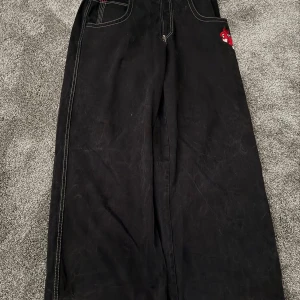  Letar efter JNCO-jeans av högsta kvalitet, jag är din kille😁 - Säljer ett par ikoniska svarta JNCO jeans med extremt wide fit och kontrastsömmar. På bakfickan finns en fet broderad detalj med röda boxningshandskar. Klassisk streetwear-vibe och riktigt rymliga ben, perfekta för dig som gillar 90-talsstil.