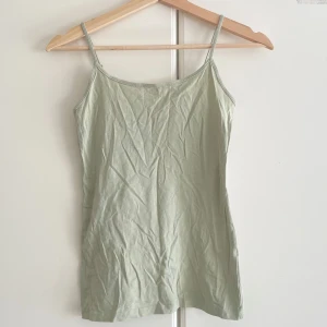 Ljusgrön linnetopp med smala axelband - Snygg ljusgrön linnetopp med smala axelband och enkel design. Toppen är ärmlös och har en rak passform som sitter skönt mot kroppen. Perfekt att styla med jeans eller shorts för en chill look. Materialet är mjukt och lätt bomull.
