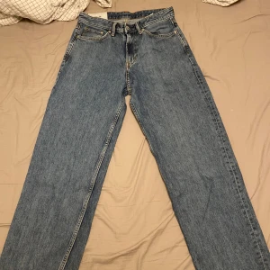 Blå loose fit jeans från H&M - Säljer ett par blå loose fit jeans från H&M i klassisk denim. Jeansen har raka ben, fem fickor och brun/orange kontrastsöm. Perfekta för dig som gillar en avslappnad och trendig look.
