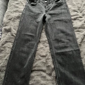 svarta raka jeans - Säljer ett par klassiska jeans i svart tvättad denim. Modellen har rak passform, fickor och knappgylf. Jeansen har en tidlös look med normal hög midja och är perfekta för dig som gillar en clean och enkel stil.