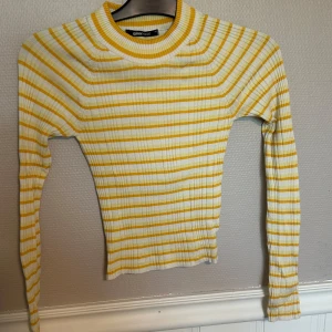 Randig ribbad tröja från Gina Tricot - Superfin ribbad tröja från Gina Tricot i vitt och gult med smala ränder. Modellen är figurnära med lång ärm och rund halsringning. Perfekt för dig som gillar färg och vill ha en fräsch look till våren eller sommaren.