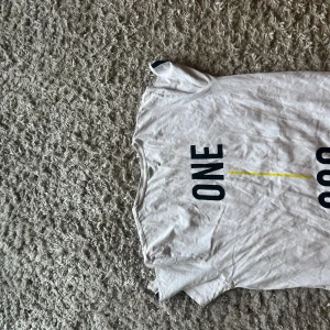 Vit t-shirt från Core med tryck - Säljer en vit t-shirt från Core i storlek XL. T-shirten har svart tryck med texten 'ONE' och 'CORE SINCE 1990 FUTURE' samt en tunn gul linje på framsidan. Klassisk rund hals och korta ärmar. Skön bomullskvalitet, perfekt till jeans eller shorts. Storleken kan passa mindre så skriv om ni har frågor