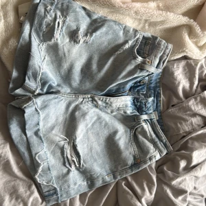Ultra high waist mom shorts i denim - Säljer ett par ljusblå mom shorts från &Denim med ultra high waist. De har slitna detaljer, råa kanter och klassisk femficksdesign. Dragkedja och knapp framtill. Perfekta för en chill och trendig look.