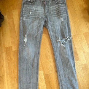 Grå slitna jeans från Dsquared2 Strl.38 - Säljer ett par grå jeans från Dsquared2 med slitningar och trasiga detaljer på benen.