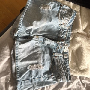 Ljusa jeansshorts från Cotonella - Snygga ljusblå jeansshorts från Cotonella med slitna detaljer framtill och klassiska fem fickor. Shortsen har normal passform, dragkedja och knapp i kopparfärg. Perfekta för varma dagar och chill stil.