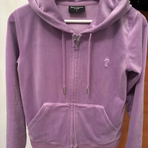 Velour hoodie, Juicy Couture - Supermjuk lila kofta från Juicy Couture i velour med dragkedja, huva och snörning. Klassisk JC-logga broderad på bröstet och fickor framtill. Perfekt för dig som älskar comfy och trendigt med en touch av 2000-talsvibe. Som ny! 