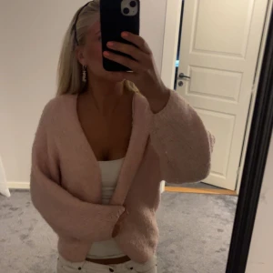 Ljusrosa stickad kofta från Lindex - Supermysig ljusrosa stickad kofta från Lindex med oversized passform och djup v-ringning. Perfekt att slänga över ett linne eller t-shirt. Koftan har långa ärmar och är riktigt fluffig och skön. Lite nopprig efter tvättar