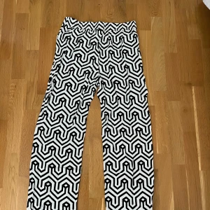 Svartvita mönstrade byxor - Säljer ett par riktigt coola byxor med svartvitt grafiskt mönster. De har raka ben och resår i midjan för extra komfort. Perfekta för dig som vill sticka ut med din stil. Materialet känns mjukt och luftigt, passar grymt till sneakers eller chunky boots. Små i storlek, detta är storlek 40. Använda ett fåtal gånger.