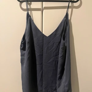 Mörkblå linnetopp från H&M - Säljer en stilren mörkblå linnetopp från H&M med smala axelband och v-ringning. Toppen är ärmlös och har en enkel, flowy passform som känns både luftig och snygg. Perfekt att matcha med jeans eller kjol för en clean look.