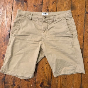 Beige bomullsshorts från NN07 - Snygga beige shorts från NN07 i mjuk bomull med lite stretch. Klassisk rak passform, midwaist och med fickor både fram och bak. Perfekta för chill dagar och har bälteshällor om du vill styla med bälte. Enkla att matcha med t-shirt eller skjorta.