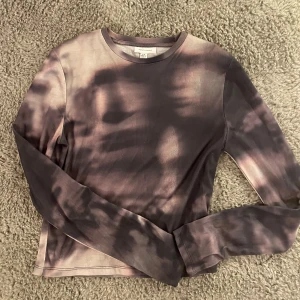Långärmad tie-dye topp från Topshop - Säljer en långärmad tröja från Topshop i coolt tie-dye likande mönster med mörklila och beige/rosa toner. Tröjan sitter tight strax över bygglinningen. Helt oanvänd.💜💞Storlek 40-42 men skulle snarare beskriva den som en 36-38. Säljer då den är för liten för mig. 🥰