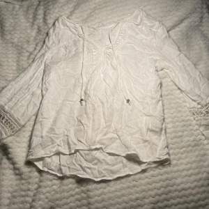 Vit blus med spetsdetaljer - Superfin vit blus med knytband och snygga virkade spetsdetaljer vid halsringning och ärmslut. Långärmad och tillverkad i ett lätt, luftigt tyg som passar perfekt till jeans eller kjol. Perfekt för alla tillfällen💕