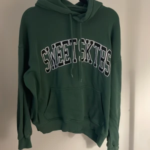 Grön hoodie - Grön hoodie från Junkyard med stor vit och svart broderad logga på bröstet. Klassisk känguruficka framtill och snörning i huvan. Mjukt bomullsmaterial.