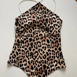 Leopardmönstrad body från H&M - Snygg baddräkt från H&M med leopardmönster i beige, brunt och svart. Modellen har tunna axelband som knyts i nacken och en klassisk, stilren passform. Perfekt för dig som vill sticka ut på stranden i sommar!
