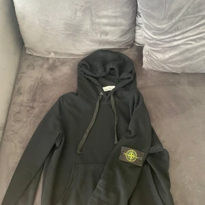 Svart hoodie från Stone Island - Svart hoodie från Stone Island med klassisk logga på ärmen. Tröjan har huva med snörning och en stor magficka. Den är för liten för mig knappt använd. Priset kan diskuteras 