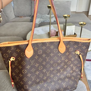 Väska  - Säljer en klassisk  handväska i brunt monogrammönster med ljusbruna skinnhandtag och detaljer. Insidan är röd med svarta ränder och har en innerficka med dragkedja. Perfekt storlek för att få plats med allt du behöver. Har inte använt den alls. Köpt på secondhand 