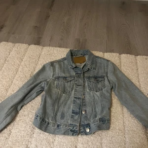 Klassisk ljusblå jeansjacka - Snygg ljusblå jeansjacka med klassisk krage och knappar framtill. Jackan har två bröstfickor med lock och långa ärmar. Perfekt för lager-på-lager och funkar året runt. Enkel att matcha med det mesta i garderoben.