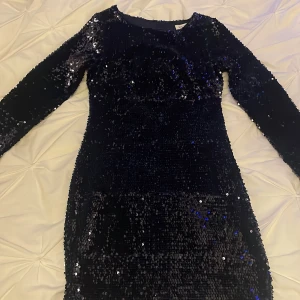 Mörkblå paljettklänning från NLY One - Snygg mörkblå kort paljettklänning från NLY One med långärmade ärmar och en djup öppen rygg. Klänningen har en tight passform och glittrande paljetter över hela ytan, perfekt för att sticka ut. Finns i storlek XS.