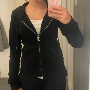 Svart velour hoodie Juicy Couture XS - Äkta svart cardigan från Juicy Couture i mjuk velour med dragkedja och huva. Klassisk logga broderad på bröstet, snörning i huvan och fickor framtill. Har gått sönder vid vänstra snöret där uppe syns inte från långt håll, även lite märken på snöret.✨✨