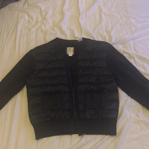 Svart pufferjacka från Gina Tricot - Säljer en svart pufferjacka från Gina Tricot i storlek 170. Jackan har quiltad framsida, två fickor och dragkedja. Ärmarna är släta och materialet känns mjukt och bekvämt. Perfekt för dig som vill ha en stilren och enkel jacka till vardags.