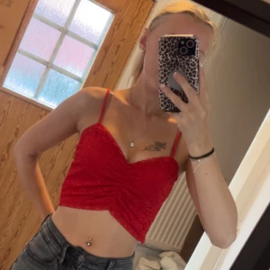 Röd croppad spetslinnetopp - Säljer en röd croppad linnetopp med tunna axelband och snygg rynkning framtill. Toppen är gjord i spetsmaterial som ger en cool och romantisk vibe. Perfekt att matcha med höga jeans för en trendig look.