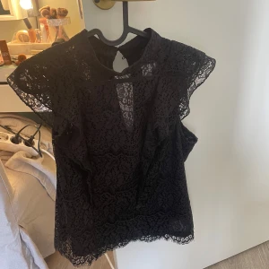 Svart spetsblus  - Säljer en svart blus i spets med v-ringning och korta ärmar. Blusen har fina spetsdetaljer och är perfekt för att lyfta en outfit. Lätt och luftig modell.