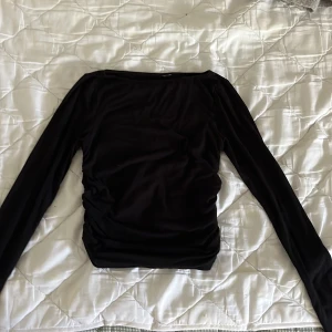 Svart långärmad topp med rynkade sidor - Säljer en svart långärmad topp med snygga rynkade detaljer på sidorna. Toppen har en enkel, stilren design med rundad halsringning och är tillverkad i ett mjukt, stretchigt material som sitter skönt på kroppen. Lappen är bortklippt men jag tror att jag har köpt den från hm❤️