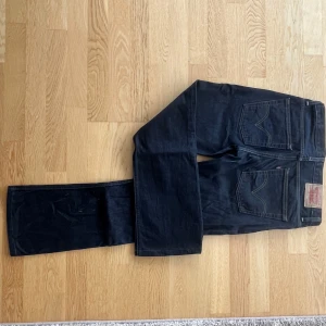 Levi's 507  mörkblå jeans straight fit - Mörkblå Levi's 507 jeans med klassisk rak passform och femficksdesign. Jeansen har tydliga kontrastsömmar, knappgylf och ikoniska bakfickor med Levi's signaturbåge. Tillverkade i robust denim som ger en tidlös look.                   I strl W33 L33 (butiksupplagda från L34)