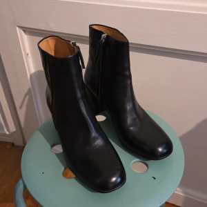 Svarta skinnstövletter från Vagabond - Snygga svarta stövletter från Vagabond i äkta skinn med läderfoder. Modellen har en rund tå, blockklack och dragkedja på sidan för enkel på- och avtagning. Perfekt till jeans eller kjol för en clean och stilren look.