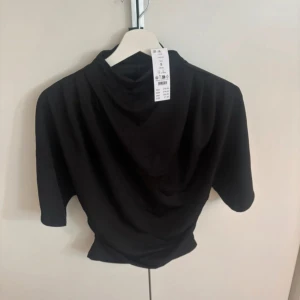 Svart t shirt tight i midjan oanvänd från Gina Tricot - Svart oanvänd t shirt från Gina Tricot som är i glansigt tyg. Den har veck på sidorna som gör att den faller väldigt fint och blir tight i midjan💕