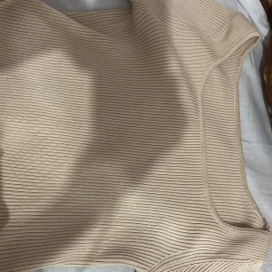 Beige ribbad topp  - Snygg beige ribbad topp  med rund halsringning. Perfekt att matcha med jeans eller kjol för en clean och stilren look. Mjuk och stretchig för en bekväm passform.