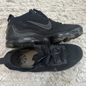 Nike Skor - Nike Air VaporMax 2021 FK sneakers i helsvart med stickad ovandel och genomskinlig, bubblig sula med färgstänk. Swoosh-logga på sidan, snörning och dragflik bak. Använda Max 2 månader, OBS kvitto finns. 