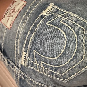 True Religion ljusblå bootcut jeans - Säljer ett par vintage ljusblåa True Religion jeans med vit brodering. Svåra att få tag på i denna modell. Strl 25 men är ganska strechiga och kan passa olika. Sitter lowrise på mig men står att de är midrise. Är 175cm lång men är för korta, skulle säga att de passar personer som är runt 168-170cm långa.  Tveka inte att höra av er vid frågor och prisförslag💕☺️