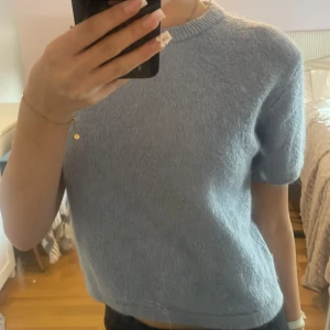 Ljusblå stickad tröja Gina Tricot - Supermysig ljusblå stickad tröja från Gina Tricot med korta ärmar och rund hals. Tröjan har en lite boxig passform och är perfekt för lager-på-lager. Mjuk och fluffig känsla, passar både till jeans och kjol.