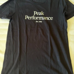 Svart Peak Performance t-shirt - Svart t-shirt från Peak Performance med vit logga och text 'Est. 1986' på bröstet. Klassisk rund hals och korta ärmar. Perfekt för en avslappnad och sportig stil.