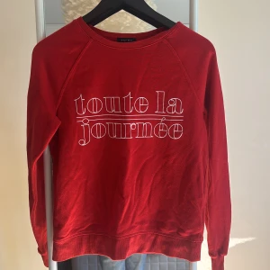 Röd sweatshirt från Amisu med tryck - Röd sweatshirt  med vit text 'toute la journée' framtill. Tröjan har rund halsringning och långa ärmar. Tillverkad i mjuk bomullsmix som är skön att ha på sig. Perfekt för en chill och avslappnad stil.