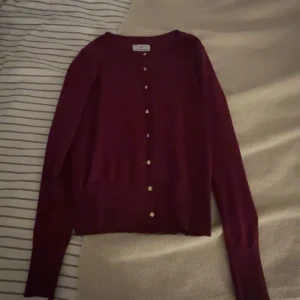 Vinröd kofta med knappar - Vinröd kofta med rund hals och långa ärmar. Stängs med små knappar framtill och har en klassisk, enkel design. Perfekt att slänga över en topp för en chill look. Mjuk och skön känsla, passar till mycket.