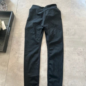 Svarta leggings med twistad midja - Svarta leggings med hög midja och snygg twistad detalj framtill. De är tighta och gjorda i ett stretchigt material som känns mjukt mot huden. Perfekta för en chill vardagslook eller när du vill ha något bekvämt men ändå stilrent.