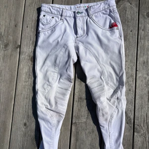 Vita ridbyxor från Animo Italy - För barn. Snygga vita ridbyxor från Animo Italy med grå kontrastsömmar och silikongrepp på insidan av benen. Klassisk femficksdesign och röd detalj vid fickan. 